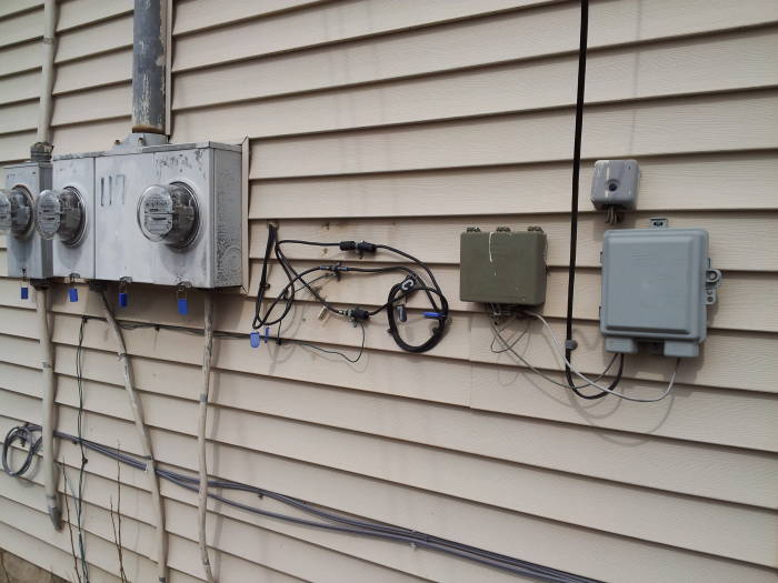 Electrical, cable, and DSL and voice telco service entrances are on the rear wall of a house.