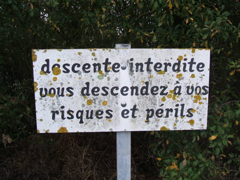 Danger sign along the cliff face near Pointe du Hoc: Access Interdite. Vous descendez a vos risques et perils.