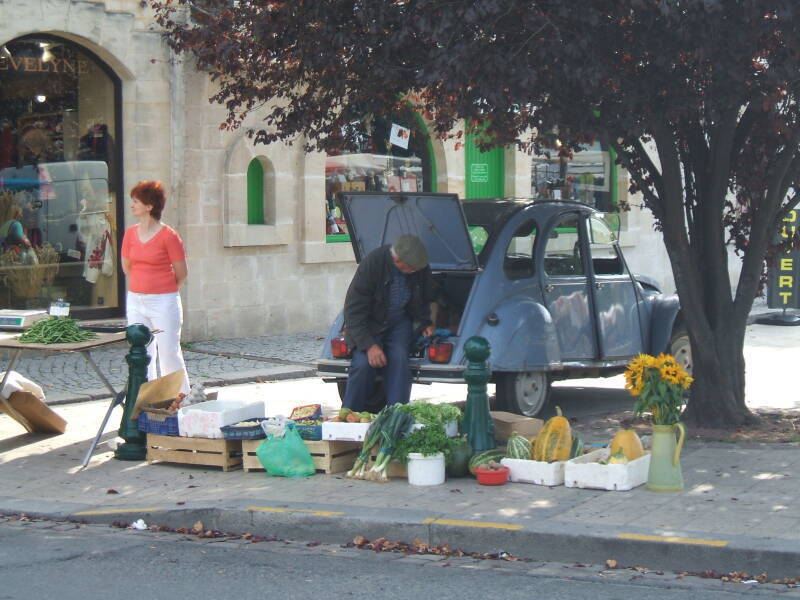 A slab-sided Citroën at the Carentan market, in Normandy.  A man sells fruits and vegetables from the rear of the car.