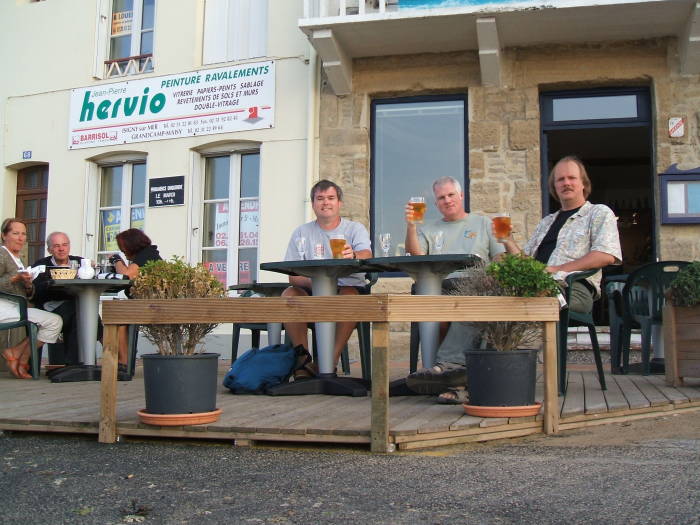 Three men drinking beer at an outdoor cafe in France.