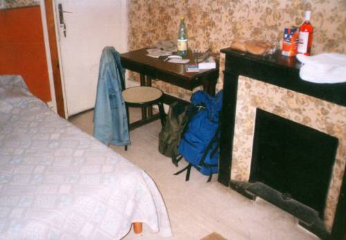 The furniture in a room just like Jim Morrison's room at l'Hôtel de Médicis in Paris: the blocked off fireplace, and a small desk and chair. The mantle holds a bottle of cheap wine, fresh bagettes, and fruit juice.