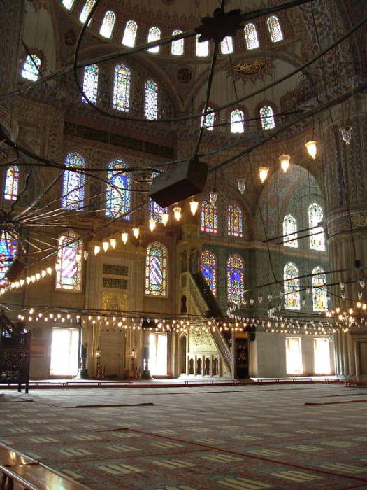 Interior of the Blue mosque or Sultanahmet Cami, in Istanbul.  Mihrab and Minbar.  Large chandeliers above many prayer rugs.