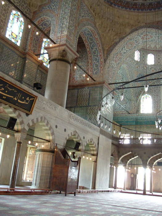 Interior of the Blue mosque or Sultanahmet Cami, in Istanbul. Mihrab and Minbar. Large chandeliers above many prayer rugs.